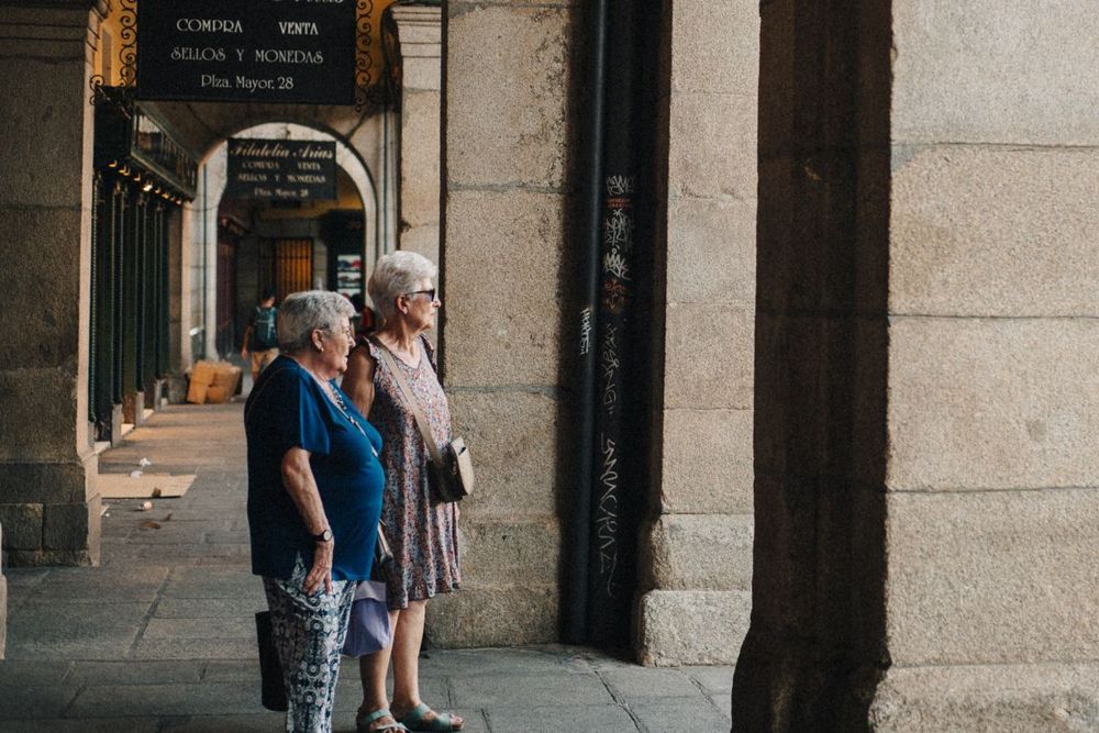 Elderly women standing in conversation under arches.