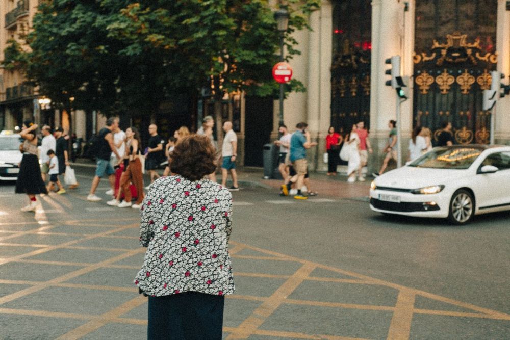 Woman standing still at a crosswalk, crowd in motion around her.